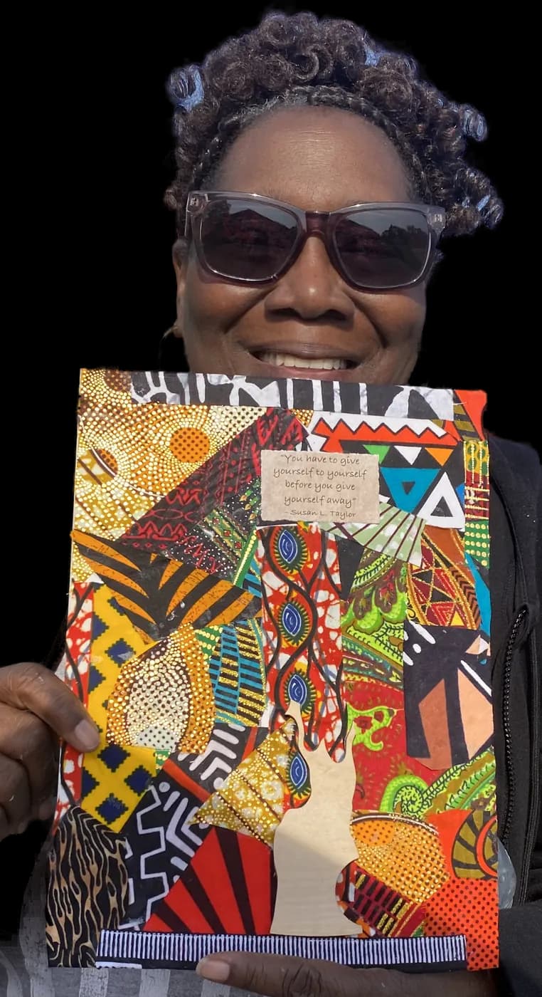 A maker in sunglasses holding up her finished fabric-collage affirmation board outside a make & take.